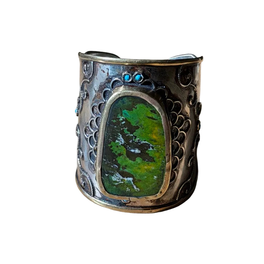 Decorative cuff bracelet with green stone and intricate design on a white background